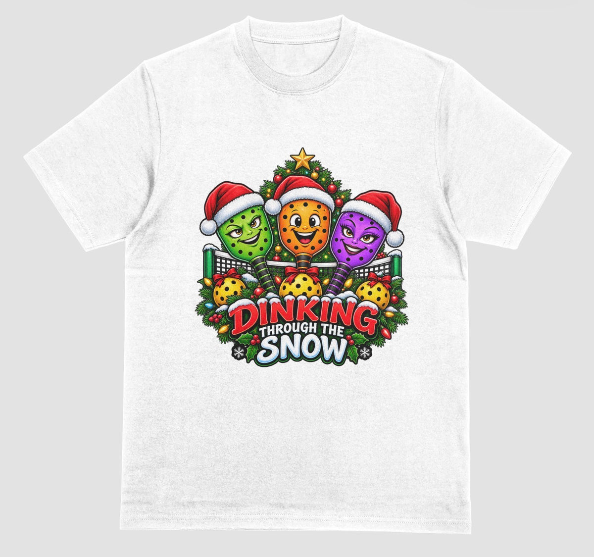A white t-shirt with “Dinking Through the Snow” Christmas design featuring pickleball paddles in Santa hats
