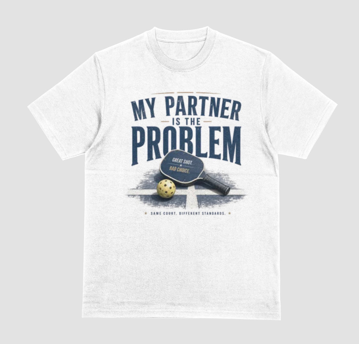 A white short-sleeve t-shirt with a vintage-style graphic on the front. The graphic features the text 'MY PARTNER IS THE PROBLEM' in dark blue, along with a paddle, ball, and net illustration.