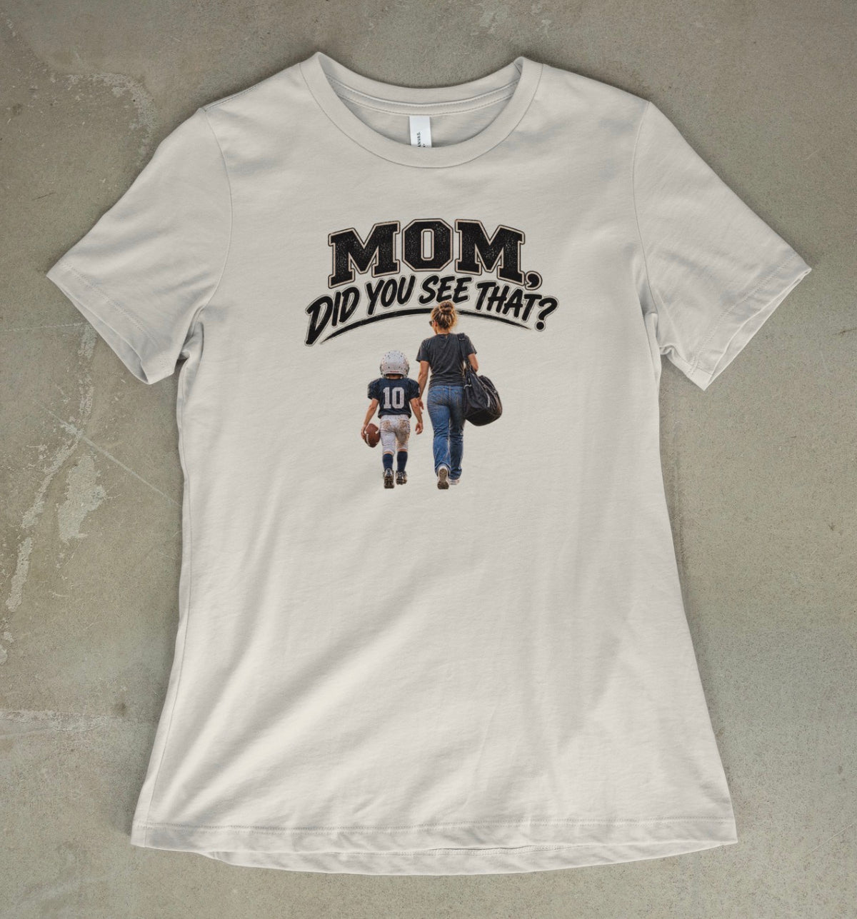 A vintage white short-sleeve t-shirt with a graphic print on the front that reads 'MOM DID YOU SEE THAT?' above an illustration of a mother and child walking away, laid flat on a textured concrete surface.