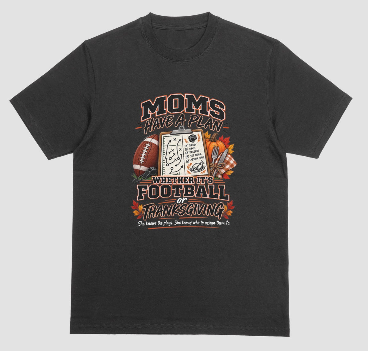 A black t-shirt featuring 'Moms Have a Plan, Whether It's Football or Thanksgiving' quote with football, clipboard playbook, pumpkin, and turkey dinner graphics"