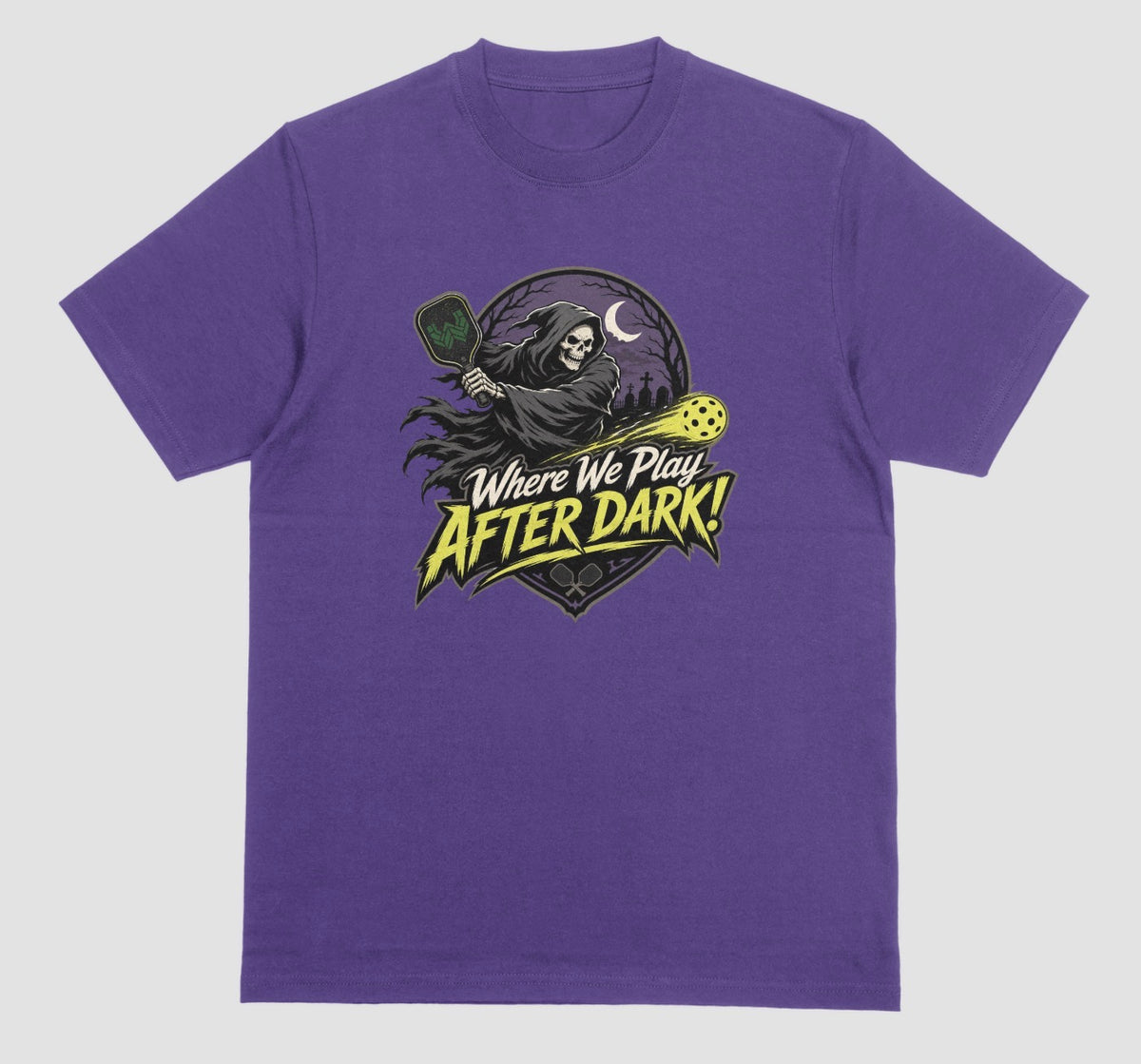 A purple t-shirt with a spooky pickleball graphic reading 'Where We Play After Dark!' showing a hooded grim reaper swinging a paddle at a glowing yellow ball.