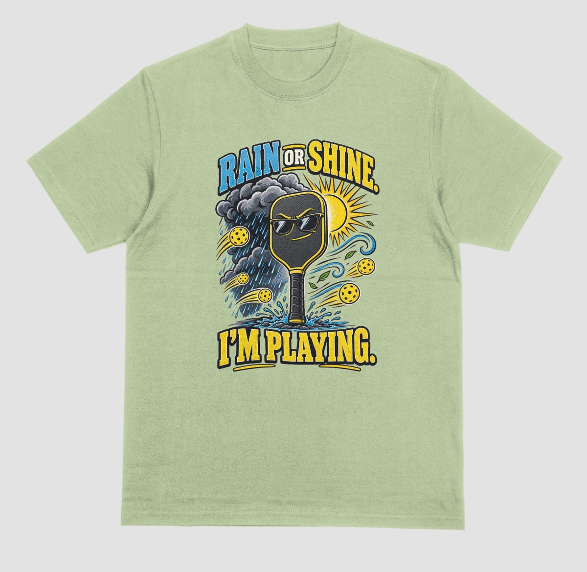 A light green Funny pickleball shirt with a sunglasses paddle, storm cloud and sun that says Rain or Shine, I’m Playing