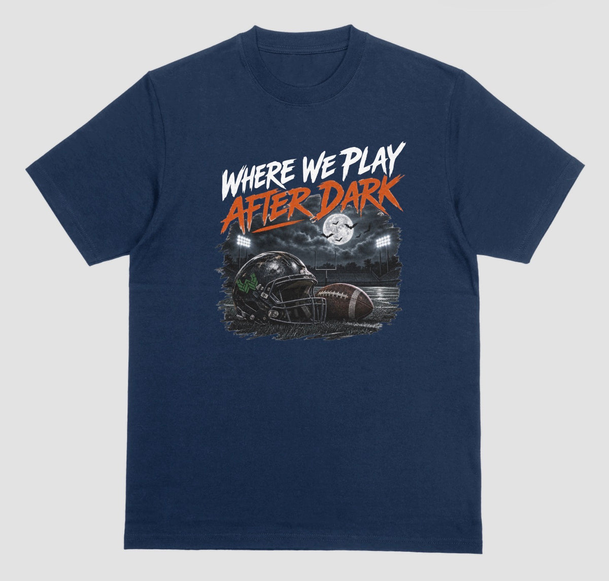 A midnight short-sleeve graphic t-shirt featuring the text 'WHERE WE PLAY AFTER DARK' in white and orange lettering above a football-themed illustration, displayed on a neutral light gray background.