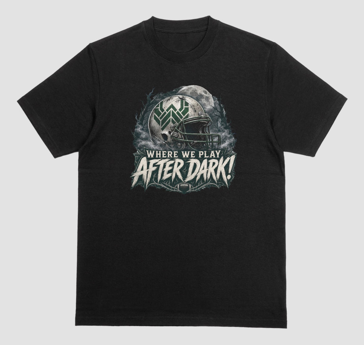 A black t-shirt with a spooky football graphic reading 'Where We Play After Dark!' showing a weathered white helmet with a green 'W' logo in front of a full moon.