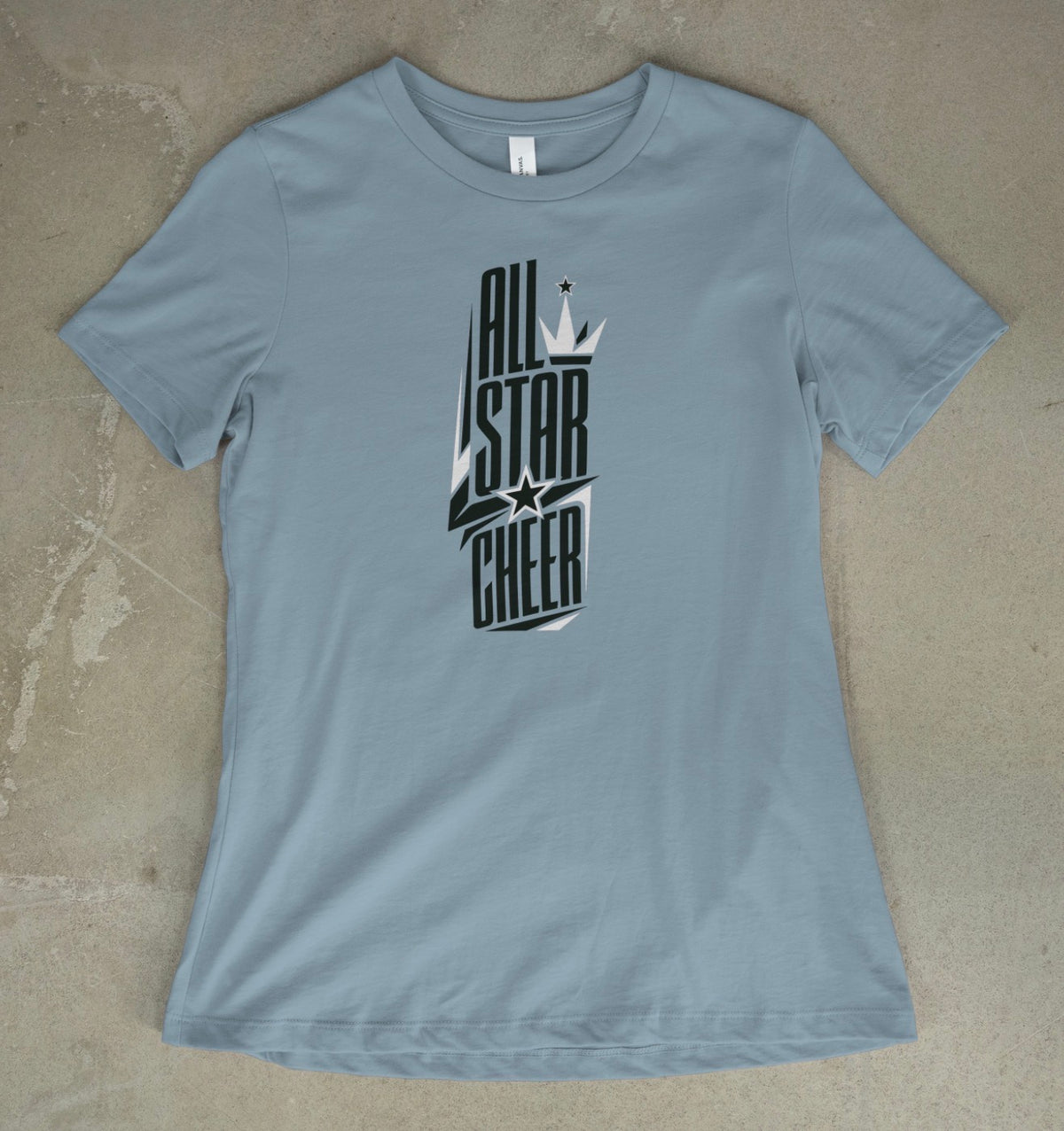 A dusty blue short-sleeve t-shirt with a black and white 'All Star Cheer' graphic on the front, laid flat on a textured gray concrete surface.
