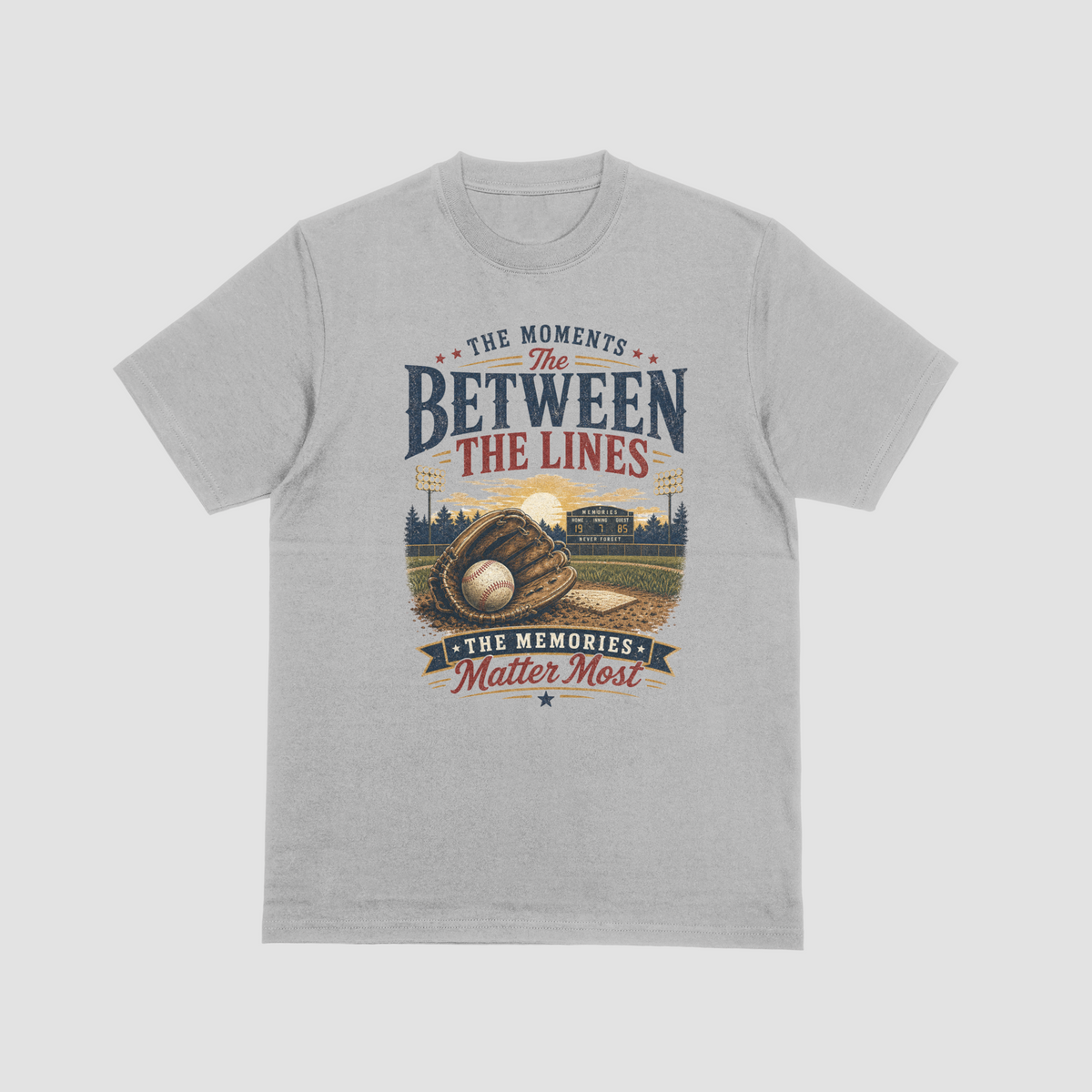 A light grey short-sleeve t-shirt featuring a baseball-themed graphic with a baseball, glove, and field, and the text “THE MOMENTS BETWEEN THE LINES & THE MEMORIES.”