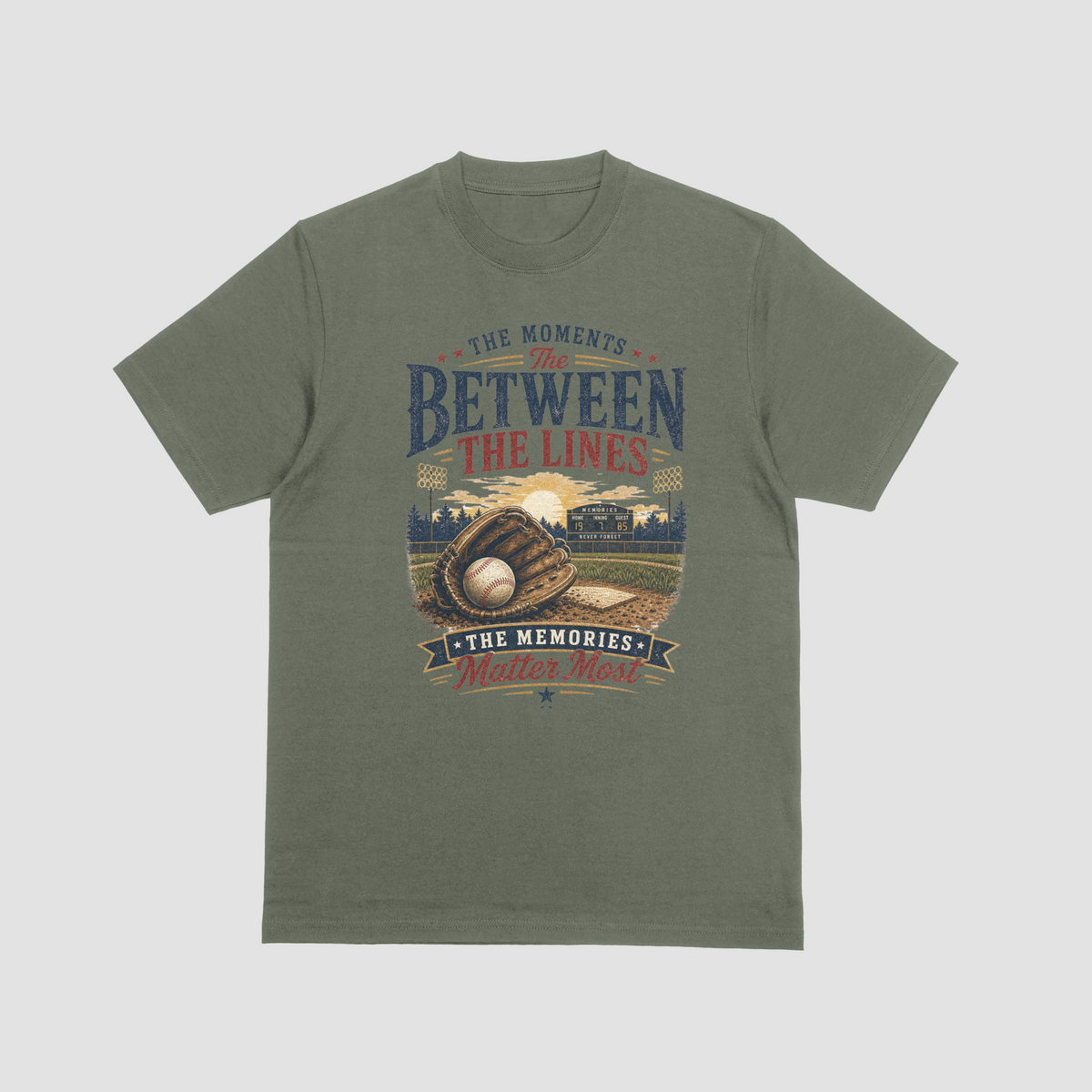 A military green short-sleeve t-shirt featuring a baseball-themed graphic with a baseball, glove, and field, and the text “THE MOMENTS BETWEEN THE LINES & THE MEMORIES.”