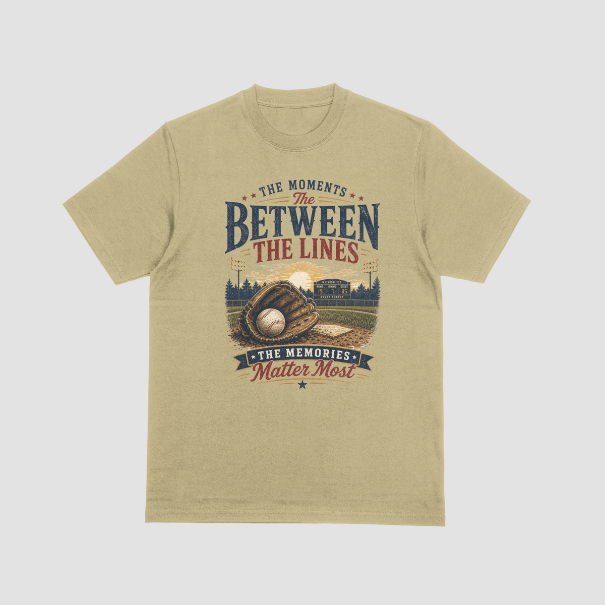 A sand color short-sleeve t-shirt featuring a baseball-themed graphic with a baseball, glove, and field, and the text “THE MOMENTS BETWEEN THE LINES & THE MEMORIES.”