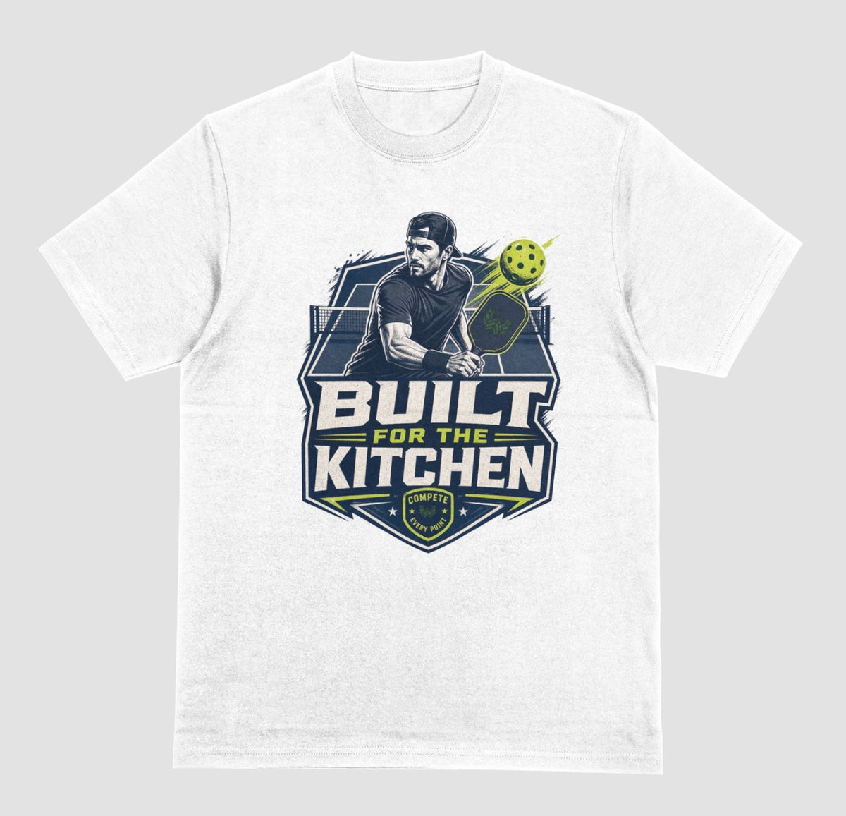 A white crewneck t-shirt featuring a large graphic print on the front. The graphic depicts a man holding a pickleball paddle with a yellow-green pickleball, above the text 'BUILT FOR THE KITCHEN' in white and yellow, with a 'SPORTS' shield logo at the bottom.