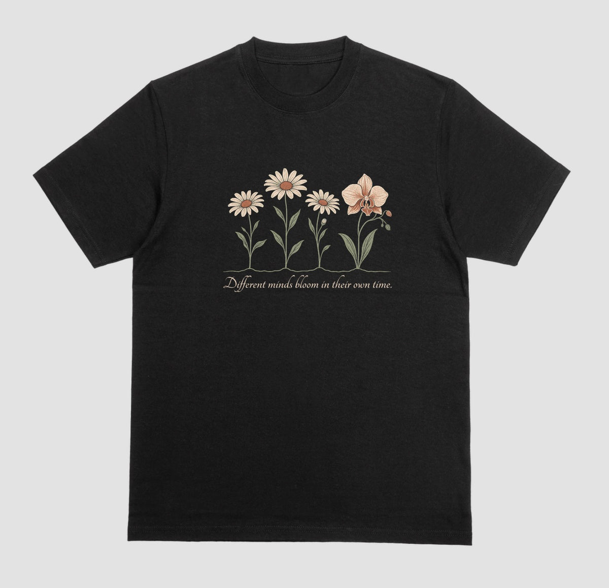 A black t-shirt with an illustration of three daisies and an orchid and the script text ‘Different minds bloom in their own time.’