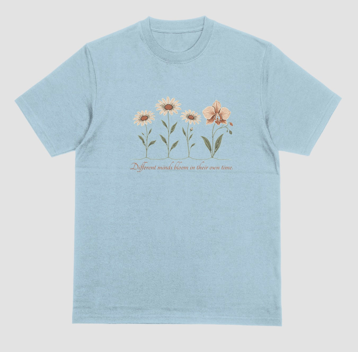A light blue t-shirt with an illustration of three daisies and an orchid and the script text ‘Different minds bloom in their own time.’