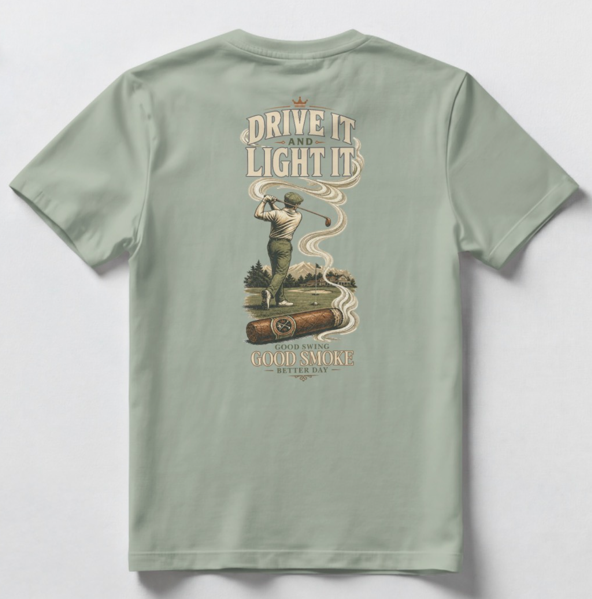 A sage green short-sleeve t-shirt shown from the back, featuring a large vintage-style graphic print with a golfer, a cigar, and the text 'DRIVE IT AND LIGHT IT' and 'GOOD SWING GOOD SMOKE BETTER DAY'.
