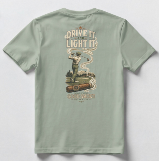 A sage green short-sleeve t-shirt shown from the back, featuring a large vintage-style graphic print with a golfer, a cigar, and the text 'DRIVE IT AND LIGHT IT' and 'GOOD SWING GOOD SMOKE BETTER DAY'.
