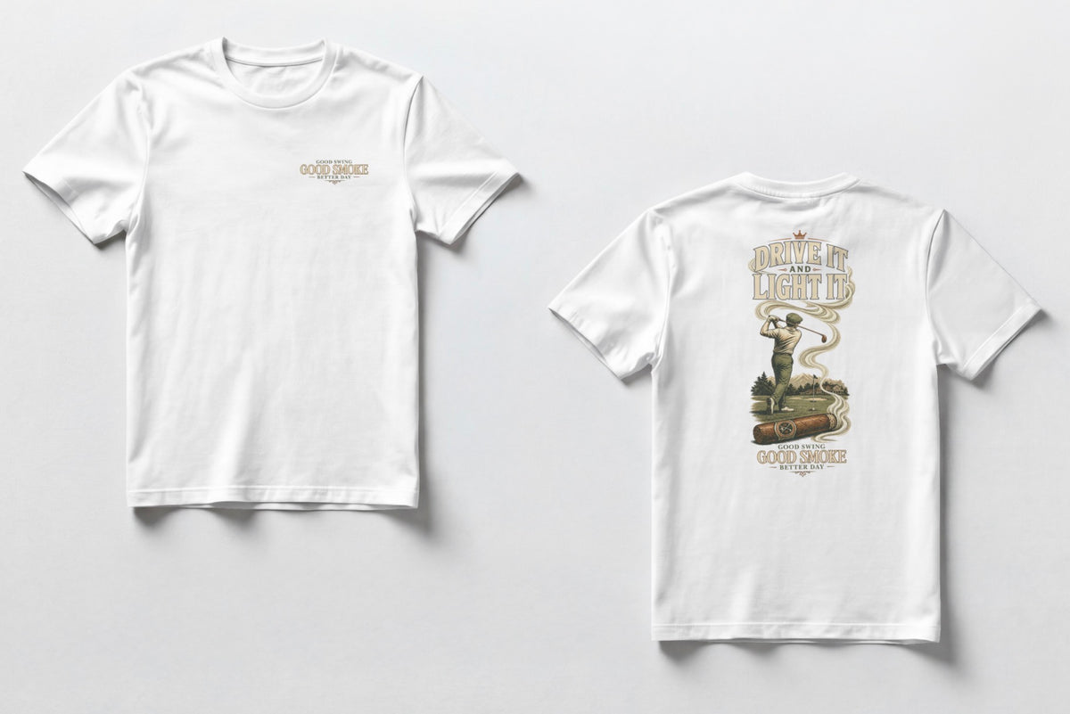 A white t-shirt, front and back views. Front chest features small text reading 'Good Swing, Good Smoke, Better Day.' Back features a large vintage-style illustration of a golfer mid-swing on a course, with a cigar in the foreground releasing swirling smoke that wraps around the text 'Drive It and Light It' at the top, with 'Good Swing, Good Smoke, Better Day' printed below the graphic.