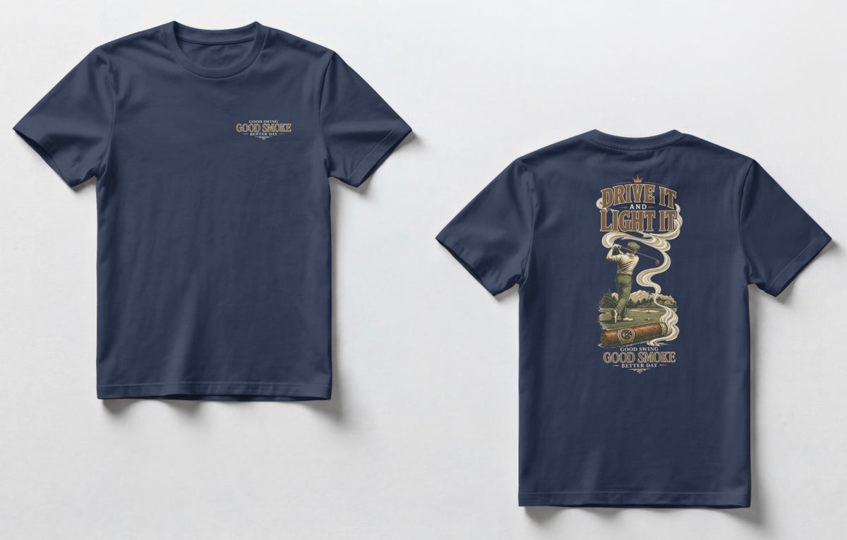 A navy blue t-shirt, front and back views. Front chest features small text reading 'Good Swing, Good Smoke, Better Day.' Back features a large vintage-style illustration of a golfer mid-swing on a course, with a cigar in the foreground releasing swirling smoke that wraps around the text 'Drive It and Light It' at the top, with 'Good Swing, Good Smoke, Better Day' printed below the graphic.