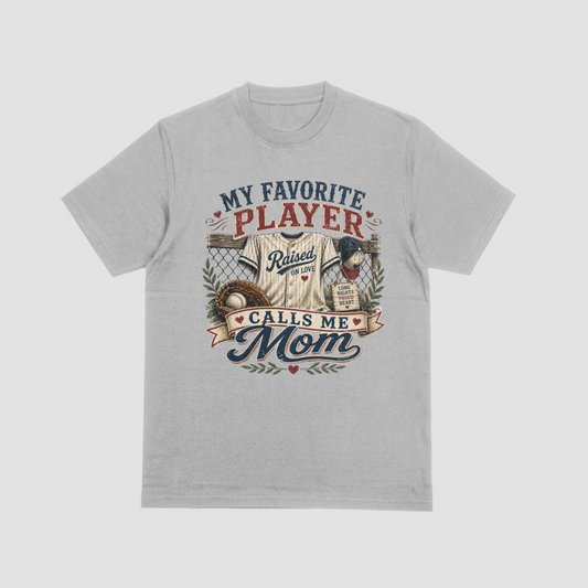 Light gray heather crewneck t-shirt featuring a baseball-themed graphic with a jersey, glove, and baseball, and the text “MY FAVORITE PLAYER CALLS ME MOM.”