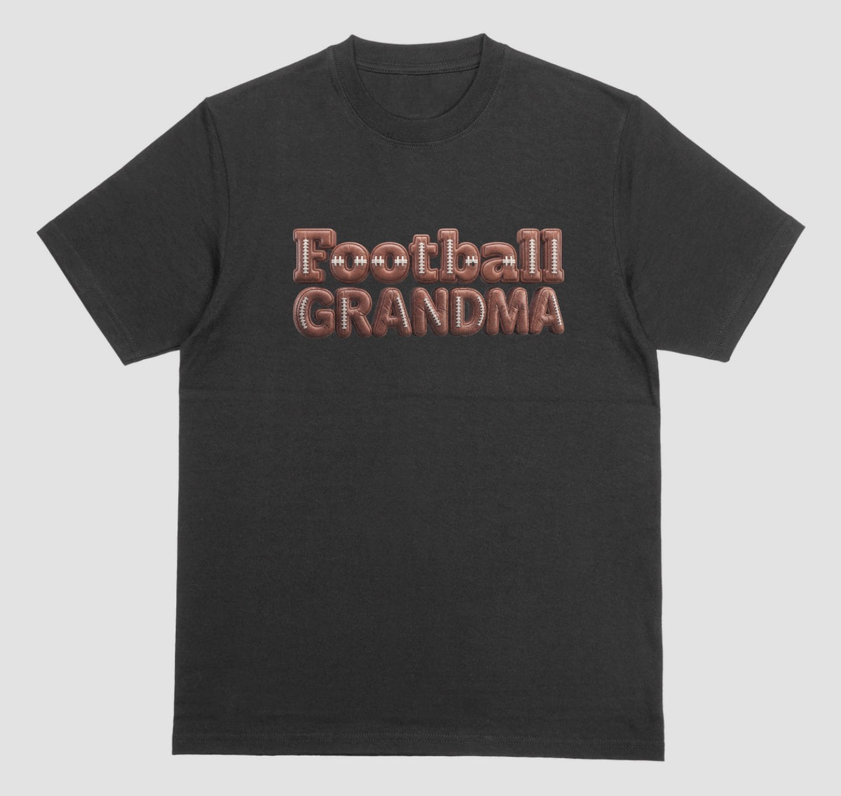 A black crewneck t-shirt featuring the words 'Football GRANDMA' printed across the chest in a 3D block font filled with a brown football leather texture and white laces.