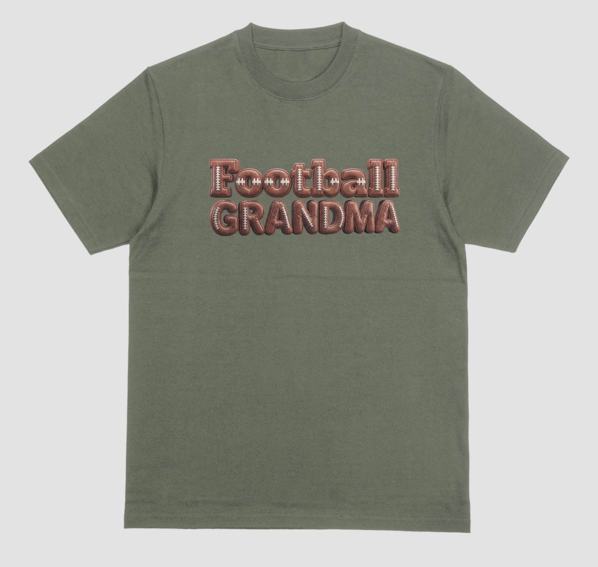 A military green crewneck t-shirt featuring the words 'Football GRANDMA' printed across the chest in a 3D block font filled with a brown football leather texture and white laces.
