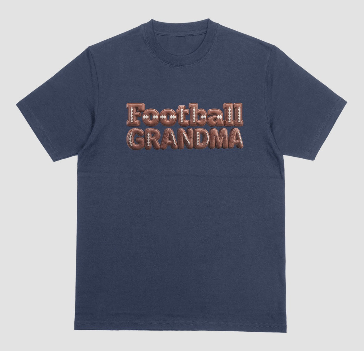 A navy blue crewneck t-shirt featuring the words 'Football GRANDMA' printed across the chest in a 3D block font filled with a brown football leather texture and white laces.