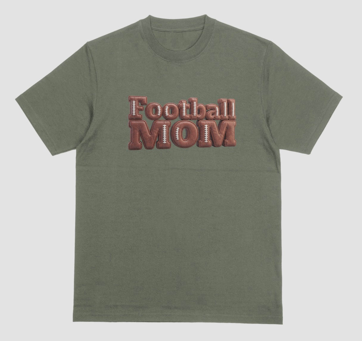 A military green crewneck t-shirt featuring a 3D-style graphic on the chest that reads 'Football MOM' in a 3D block font filled with a brown football leather texture and white laces.