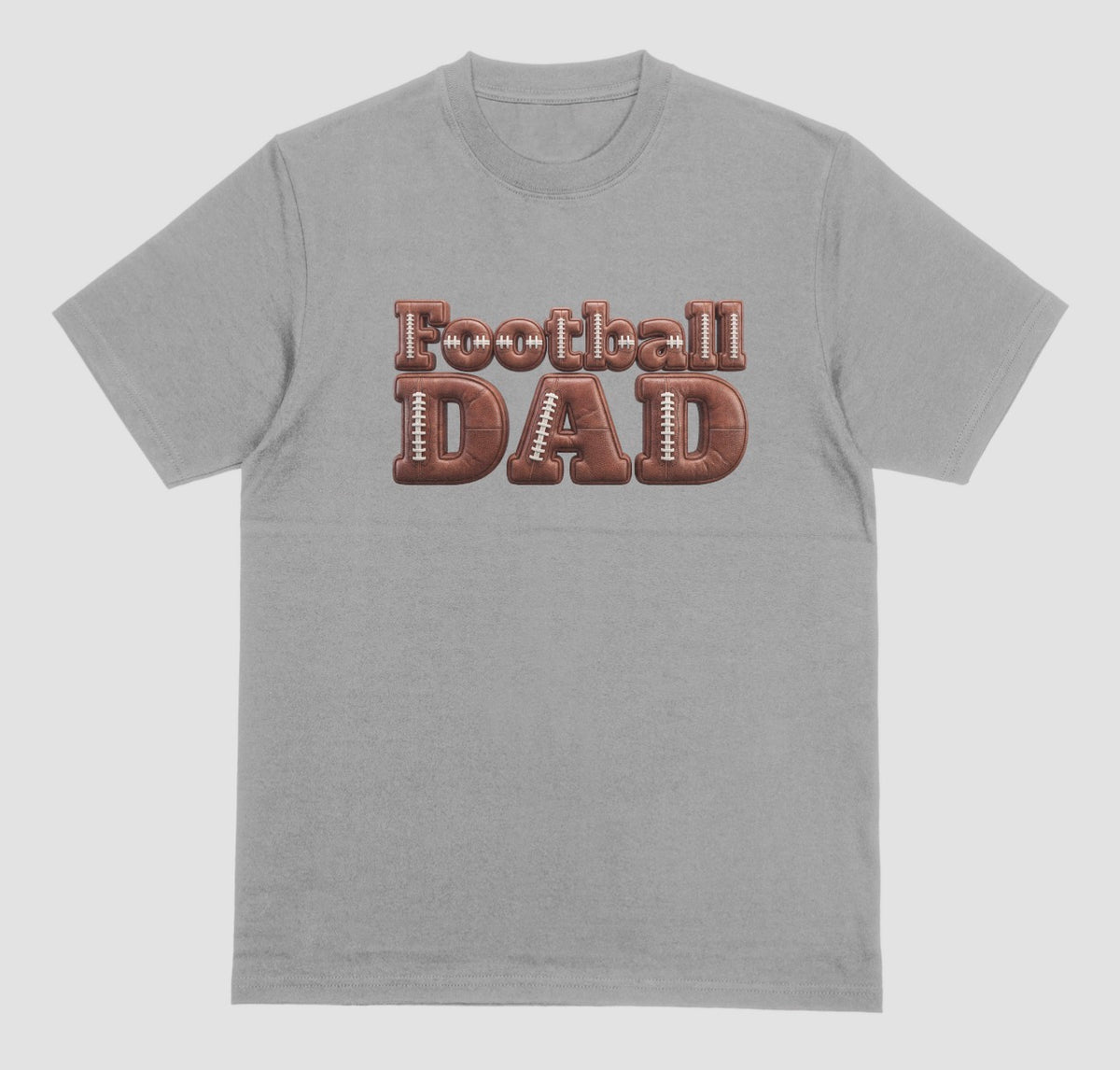 A grey crewneck t-shirt featuring a graphic on the chest that reads 'Football DAD' in a 3D block font filled with a brown football leather texture and white laces.