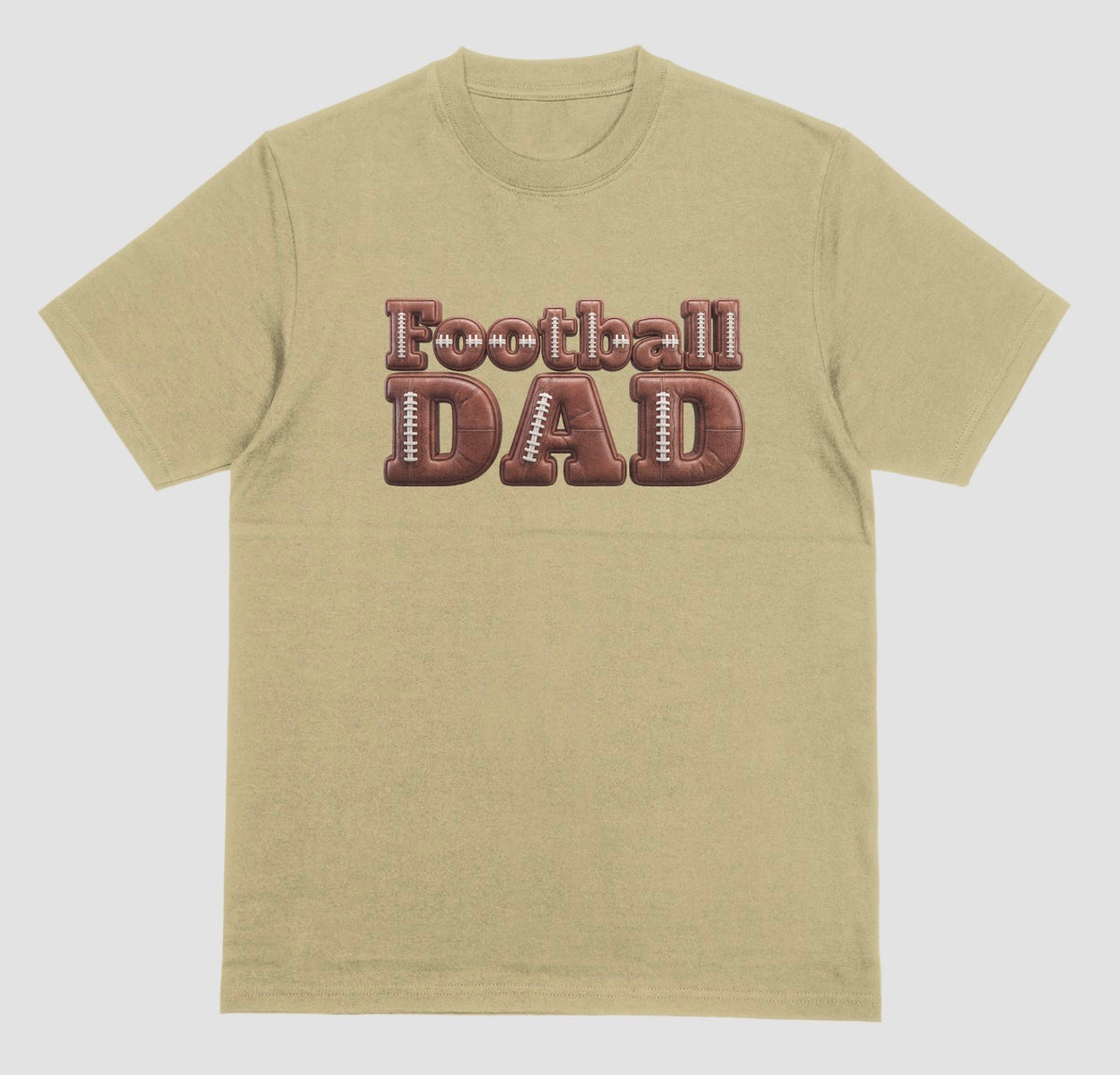 A sand color crewneck t-shirt featuring a graphic on the chest that reads 'Football DAD' in a 3D block font filled with a brown football leather texture and white laces.