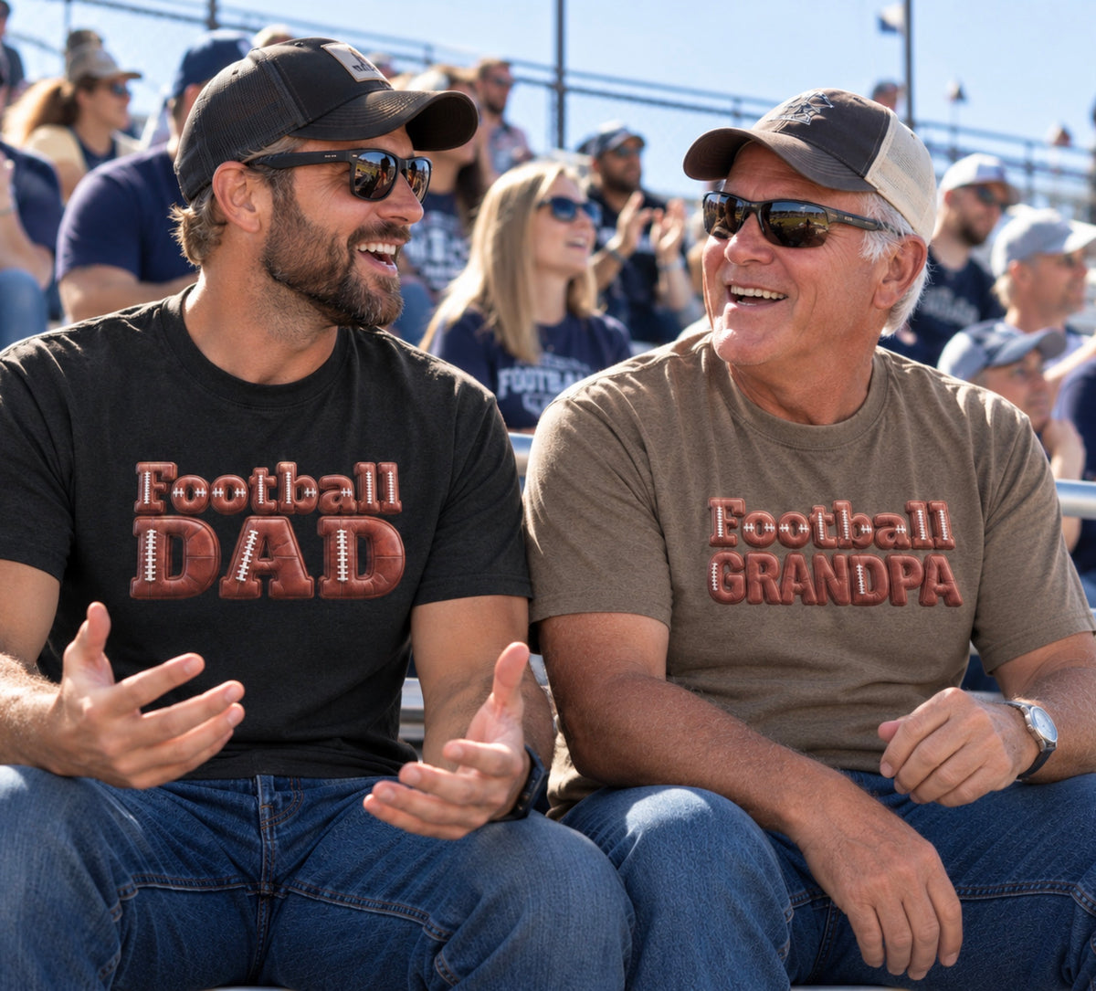 Dad and Grandpa sitting in stadium seating wearing matching graphic T-shirts. The dad on the left wears a black shirt with 'Football DAD' in a 3D block font filled with a brown football leather texture and white laces, and the grandpa on the right wears a brown savanna shirt with 'Football GRANDPA' in a 3D block font filled with a brown football leather texture and white laces.