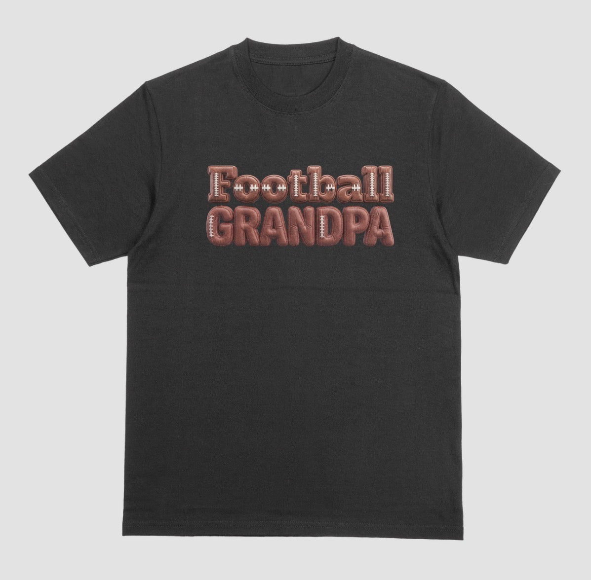 A black crewneck t-shirt featuring the words 'Football GRANDPA' printed across the chest in a 3D block font filled with a brown football leather texture and white laces.