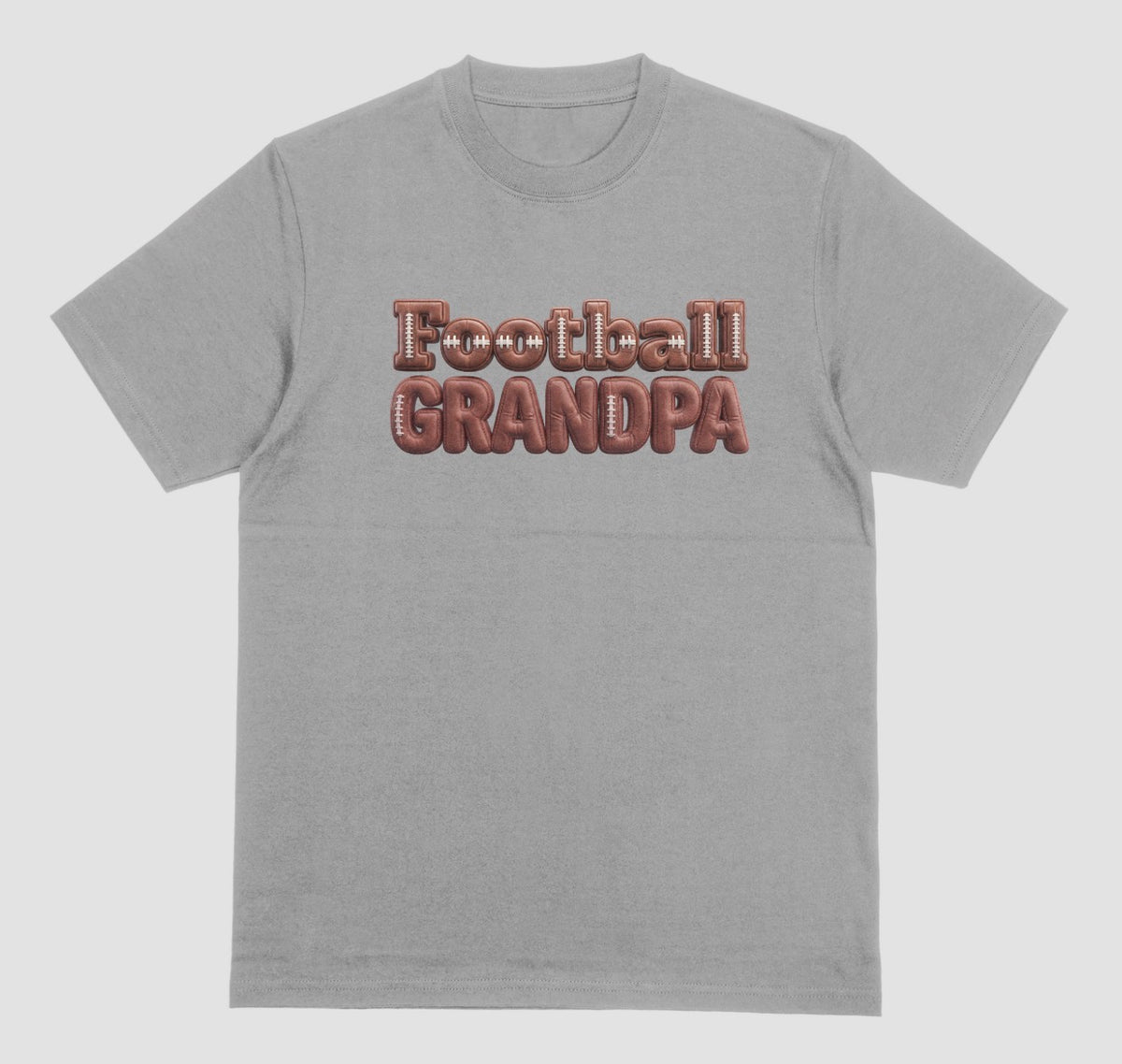 A grey crewneck t-shirt featuring the words 'Football GRANDPA' printed across the chest in a 3D block font filled with a brown football leather texture and white laces.