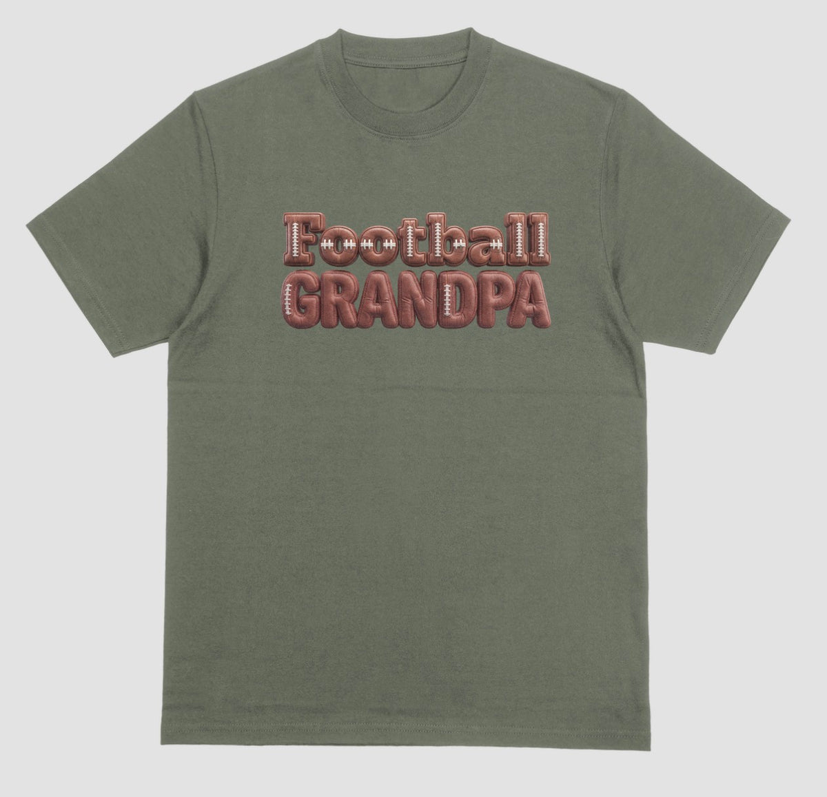 A military green crewneck t-shirt featuring the words 'Football GRANDPA' printed across the chest in a 3D block font filled with a brown football leather texture and white laces.