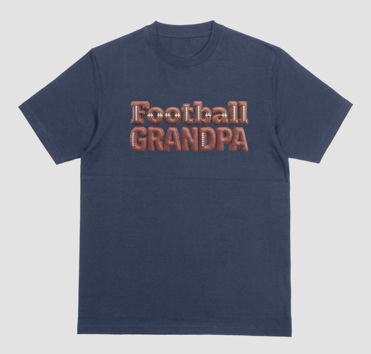 A navy blue crewneck t-shirt featuring the words 'Football GRANDPA' printed across the chest in a 3D block font filled with a brown football leather texture and white laces.