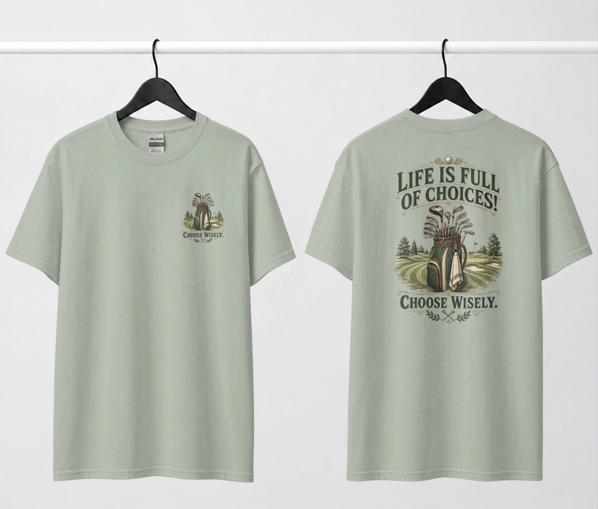 A sage green short-sleeve t-shirt shown from both the front and back, hanging on black hangers against a white wall. The design features a vintage-style illustration of a golf bag filled with clubs on a golf course, framed by the text 'LIFE IS FULL OF CHOICES! CHOOSE Wisely.