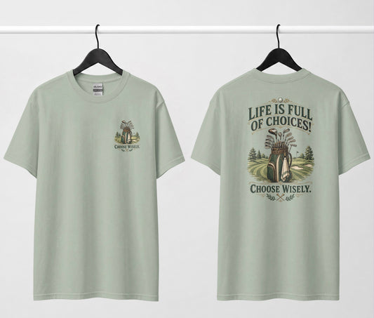 A sage green short-sleeve t-shirt shown from both the front and back, hanging on black hangers against a white wall. The design features a vintage-style illustration of a golf bag filled with clubs on a golf course, framed by the text 'LIFE IS FULL OF CHOICES! CHOOSE Wisely.