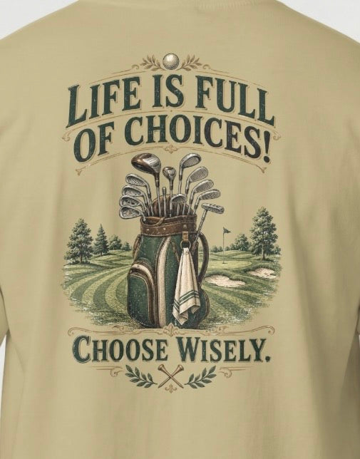 A close-up of a Sand color graphic t-shirt showing the back print. The design features a vintage-style illustration of a golf bag filled with clubs on a golf course, framed by the text 'LIFE IS FULL OF CHOICES! CHOOSE Wisely.