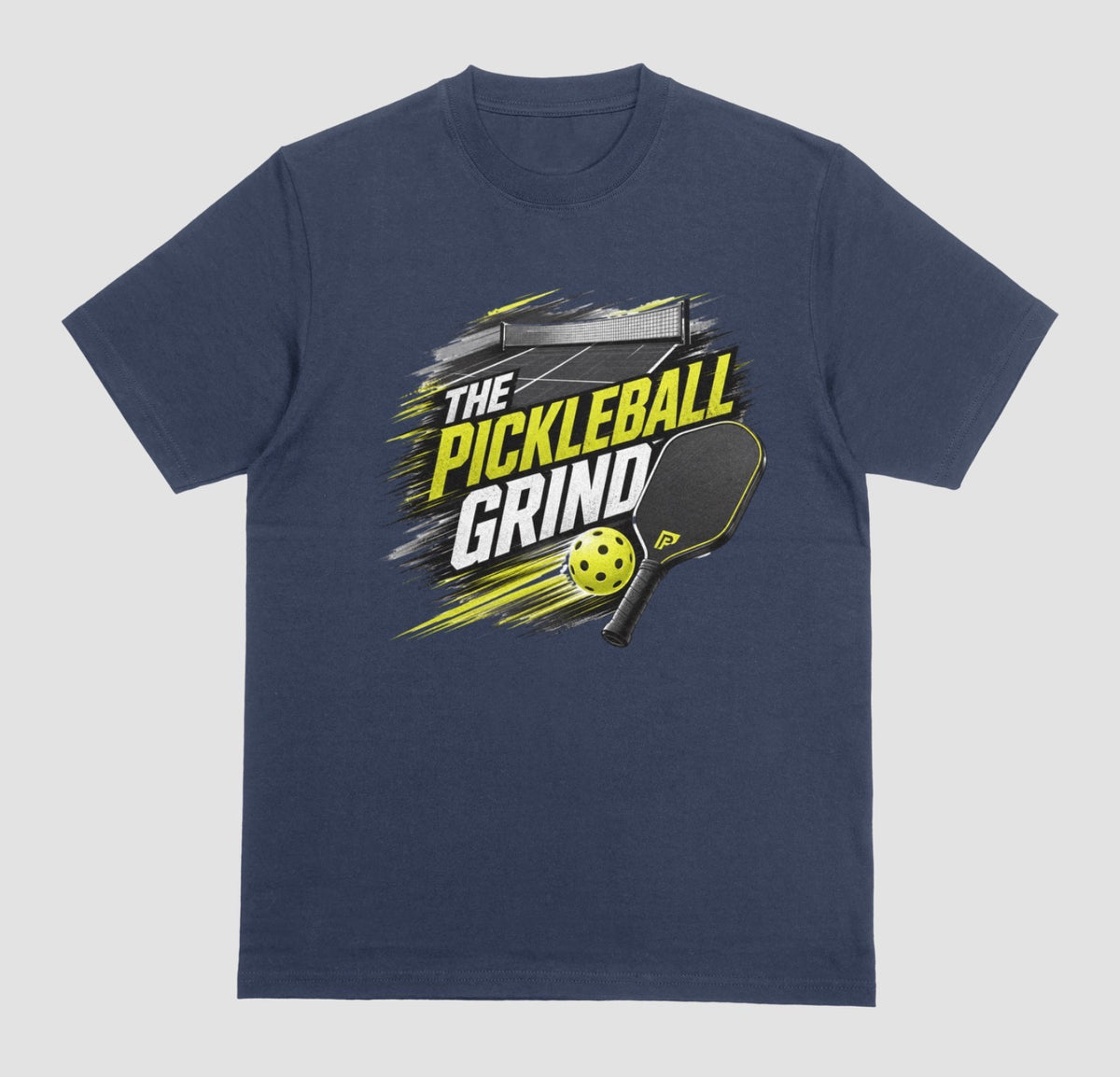 A navy blue short-sleeve t-shirt with a 'The Pickleball Grind' graphic on the chest, featuring a yellow pickleball, black paddle, and yellow/black text over a gray brushstroke design, shown on a light gray background.