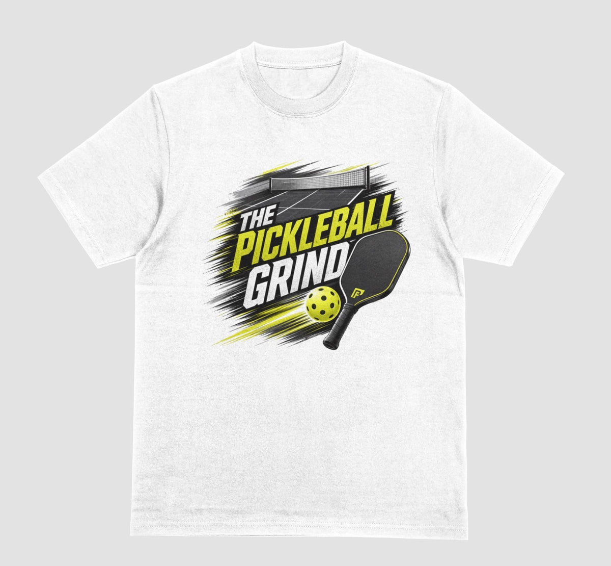 A white short-sleeve t-shirt with a 'The Pickleball Grind' graphic on the chest, featuring a yellow pickleball, black paddle, and yellow/black text over a gray brushstroke design, shown on a light gray background.