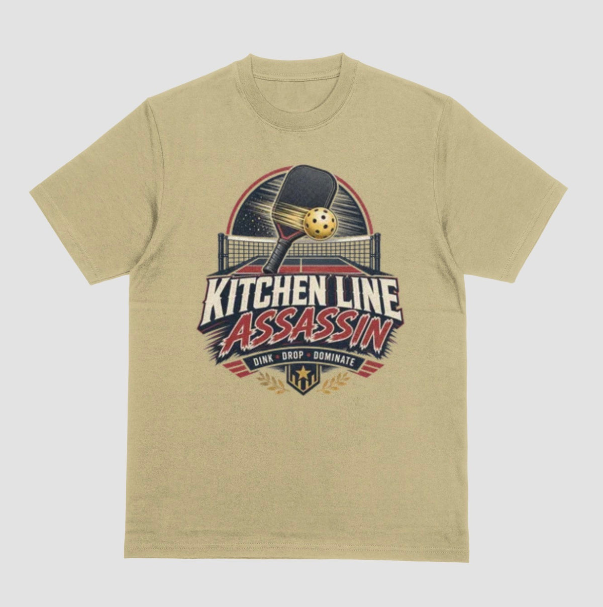 A sand color crewneck t-shirt featuring a graphic print on the front with a pickleball paddle and ball above the text 'KITCHEN LINE ASSASSIN' and 'DINK - DROP - DOMINATE'.