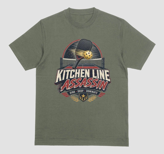 An military green crewneck t-shirt featuring a graphic print on the front with a pickleball paddle and ball above the text 'KITCHEN LINE ASSASSIN' and 'DINK - DROP - DOMINATE'.