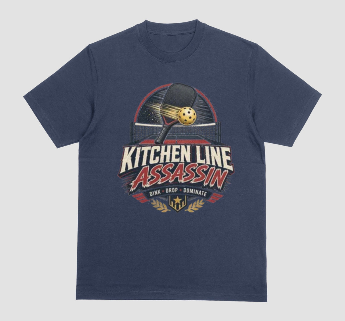 A navy blue crewneck t-shirt featuring a graphic print on the front with a pickleball paddle and ball above the text 'KITCHEN LINE ASSASSIN' and 'DINK - DROP - DOMINATE'.