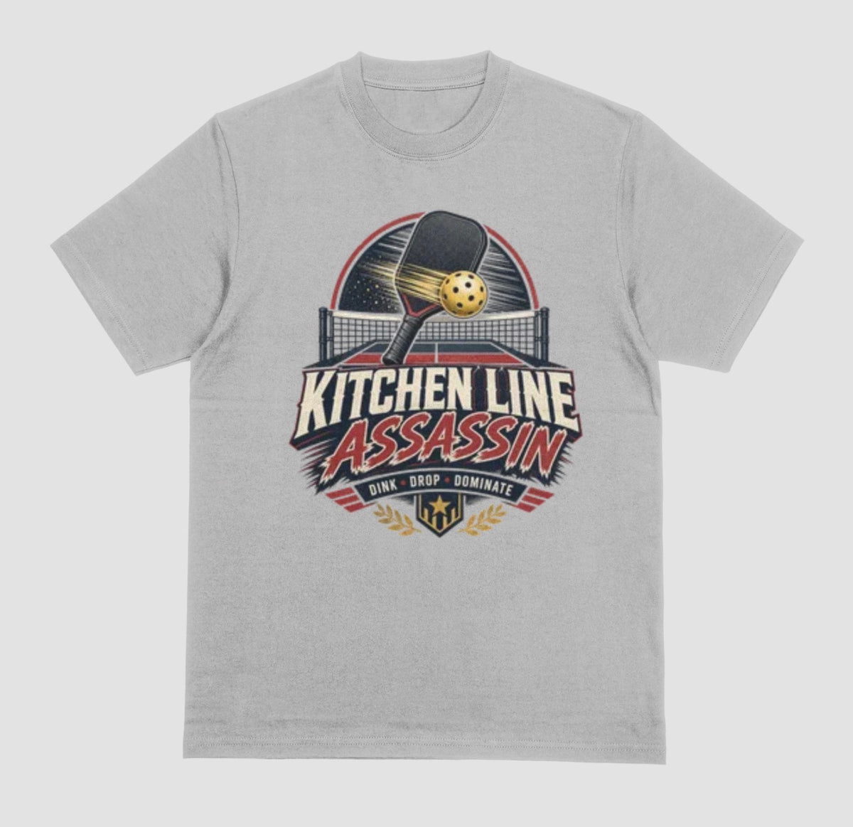 A gray crewneck t-shirt featuring a graphic print on the front with a pickleball paddle and ball above the text 'KITCHEN LINE ASSASSIN' and 'DINK - DROP - DOMINATE'.