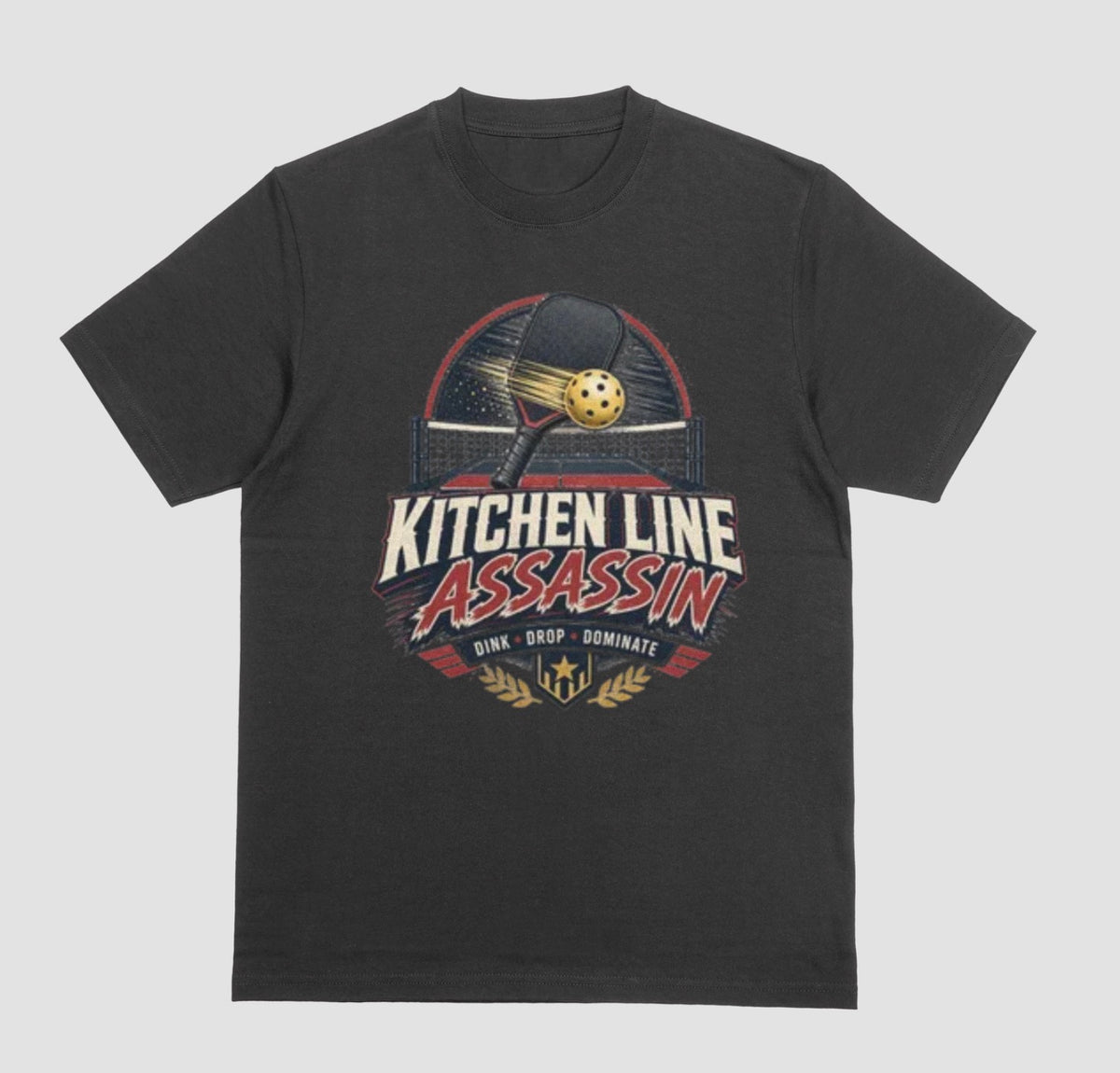 A black crewneck t-shirt featuring a graphic print on the front with a pickleball paddle and ball above the text 'KITCHEN LINE ASSASSIN' and 'DINK - DROP - DOMINATE'.