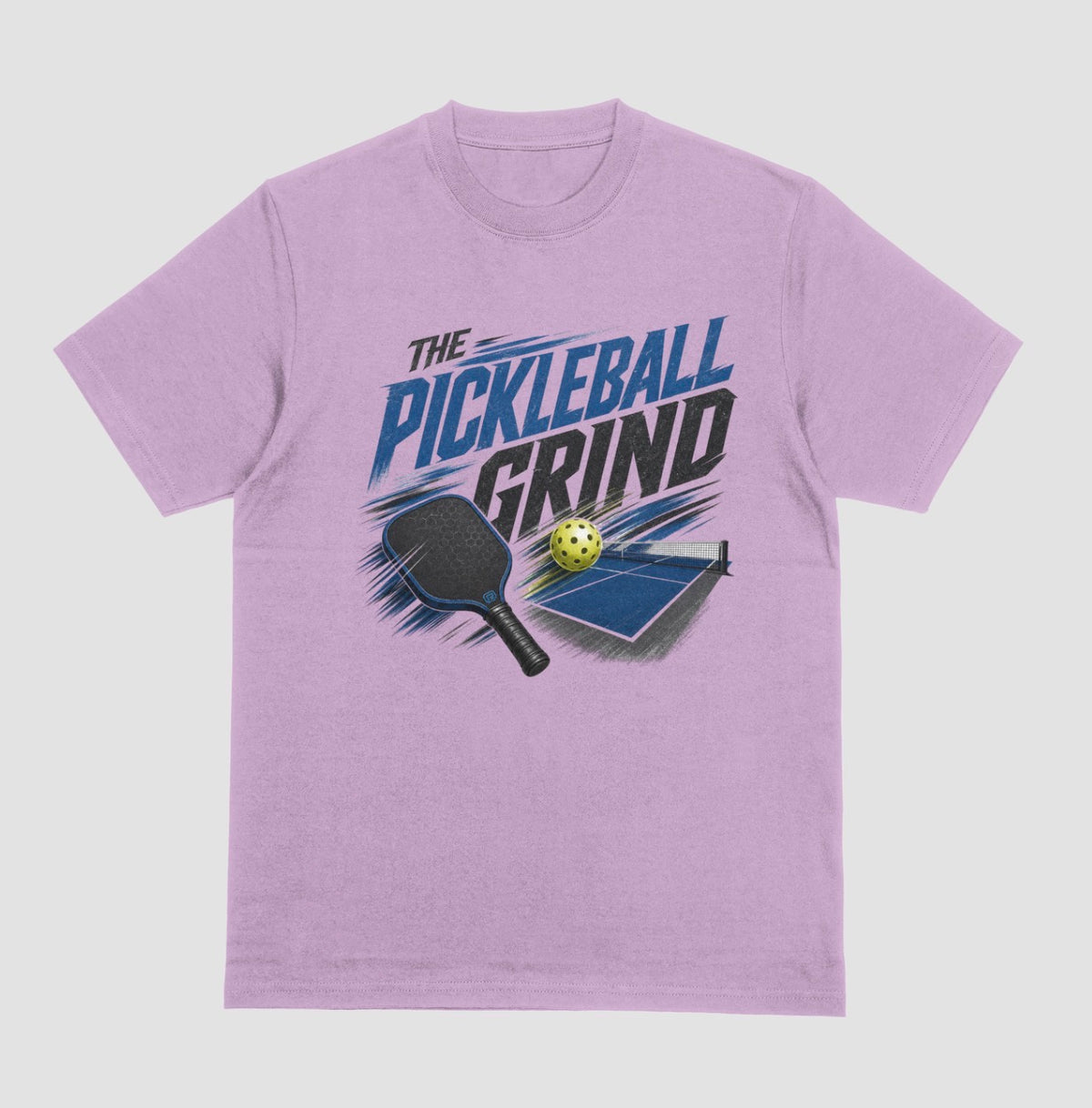 A lilac short-sleeve t-shirt with a graphic on the front that reads 'THE PICKLEBALL GRIND' in blue and black, accompanied by illustrations of a pickleball paddle, ball, and table.