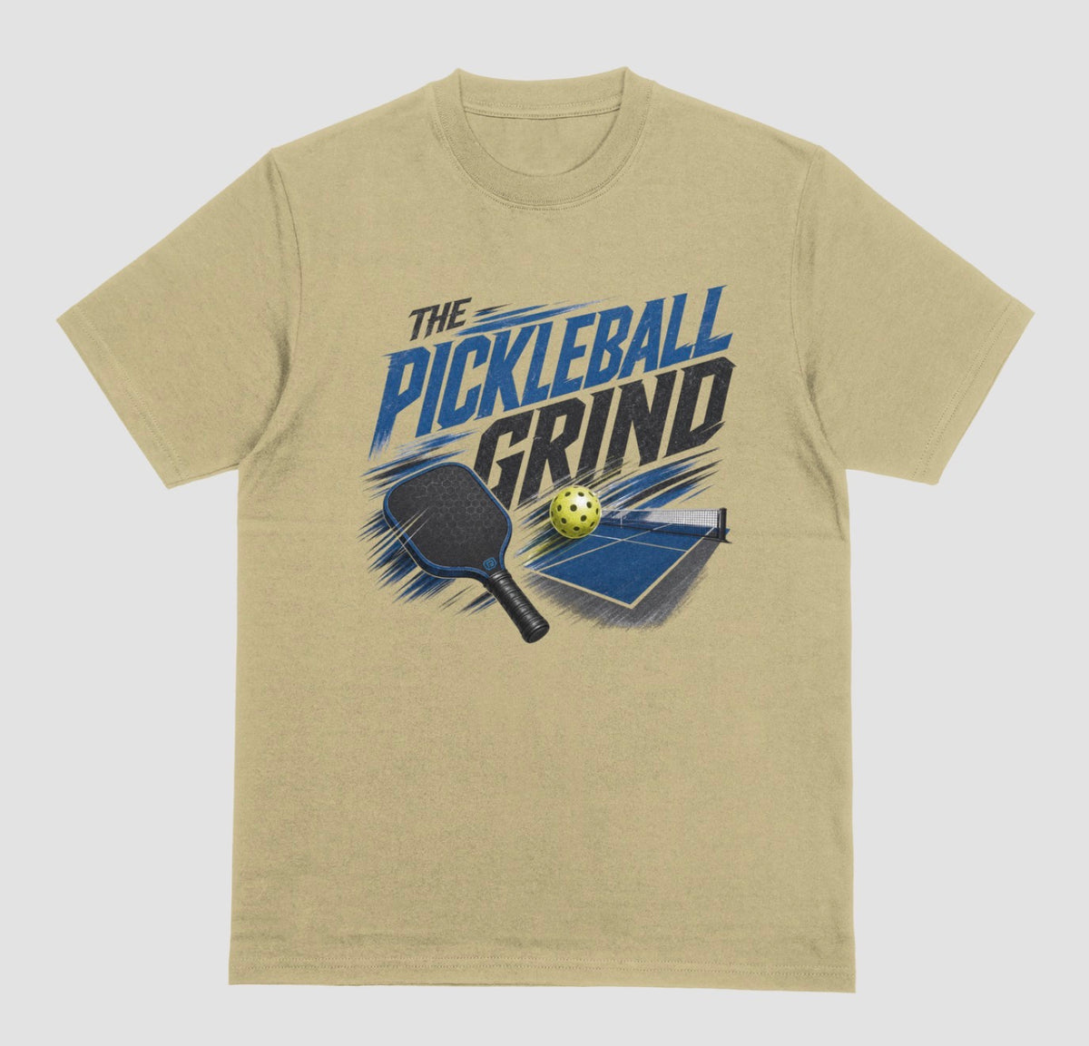 A sand color short-sleeve t-shirt with a graphic on the front that reads 'THE PICKLEBALL GRIND' in blue and black, accompanied by illustrations of a pickleball paddle, ball, and table.