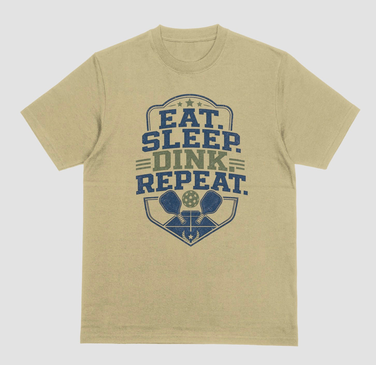 A sand color crewneck t-shirt featuring a distressed graphic on the front with the text 'EAT. SLEEP. DINK. REPEAT.'