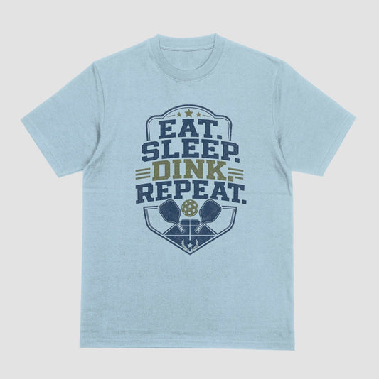 A light blue heather crewneck t-shirt featuring a distressed graphic on the front with the text 'EAT. SLEEP. DINK. REPEAT.'