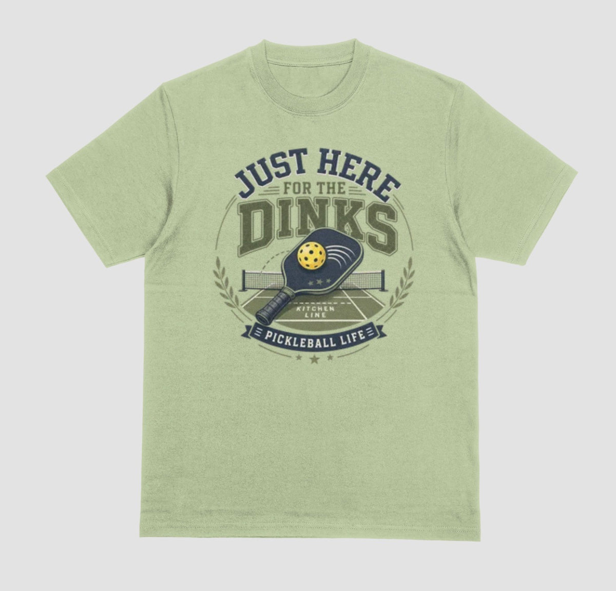A pistachio green t-shirt with a vintage-style graphic on the chest that reads 'JUST HERE FOR THE DINKS' and 'PICKLEBALL LIFE!' around an illustration of a paddle, ball, and court.