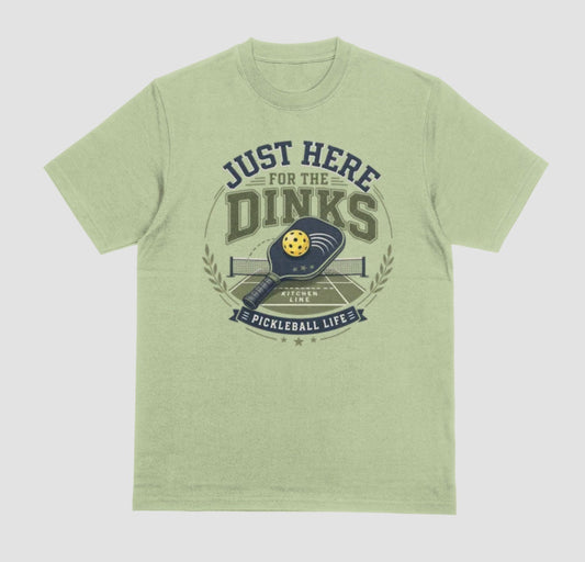 A pistachio green t-shirt with a vintage-style graphic on the chest that reads 'JUST HERE FOR THE DINKS' and 'PICKLEBALL LIFE!' around an illustration of a paddle, ball, and court.