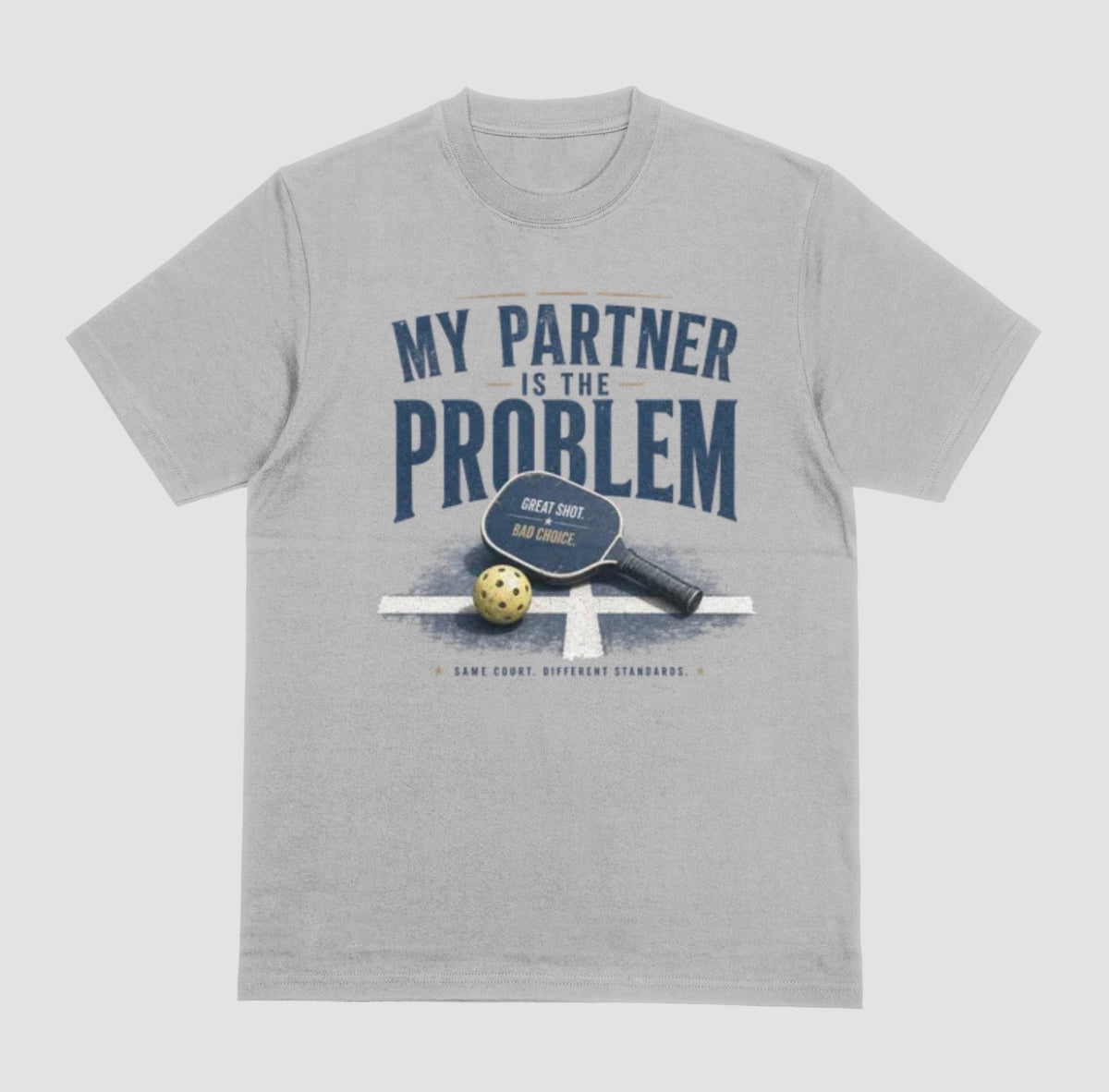 A gray short-sleeve t-shirt with a vintage-style graphic on the front. The graphic features the text 'MY PARTNER IS THE PROBLEM' in dark blue, along with a paddle, ball, and net illustration.