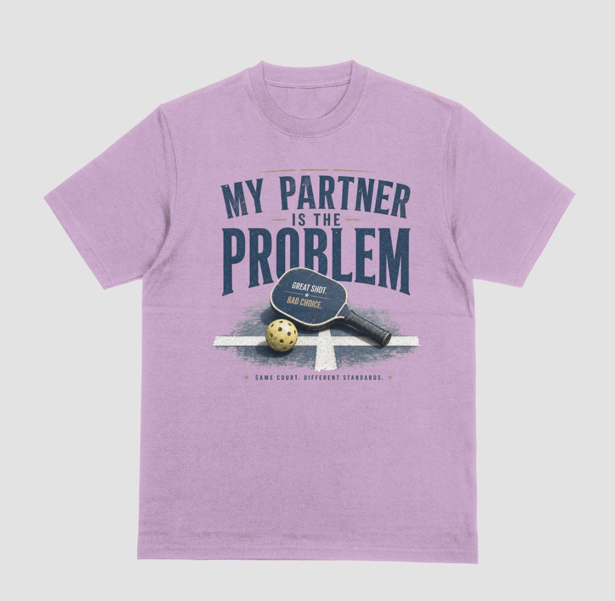 A lilac short-sleeve t-shirt with a vintage-style graphic on the front. The graphic features the text 'MY PARTNER IS THE PROBLEM' in dark blue, along with a paddle, ball, and net illustration.