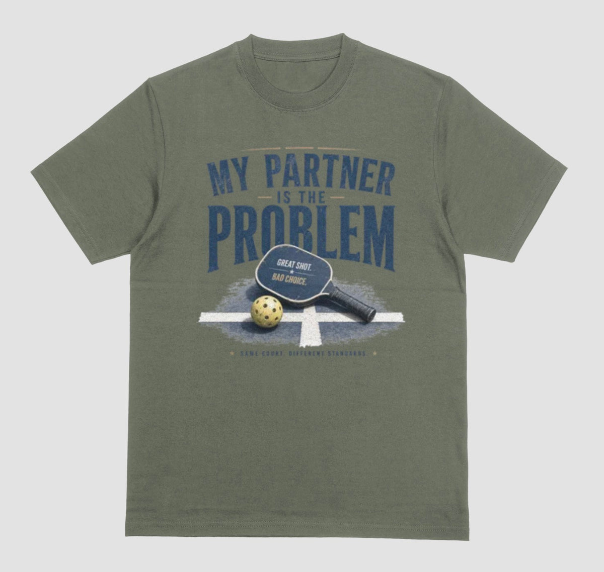 A military green short-sleeve t-shirt with a vintage-style graphic on the front. The graphic features the text 'MY PARTNER IS THE PROBLEM' in dark blue, along with a paddle, ball, and net illustration.